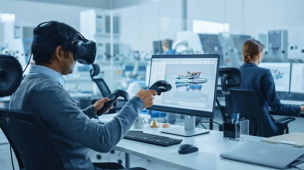 最新の産業工場:仮想現実ヘッドセットを装着した機械エンジニア、コントローラを保持し、コンピュータ上のCADソフトウェアで産業デザイン、開発、プロトタイピングのためのVR技術を使用しています。. — ストック写真