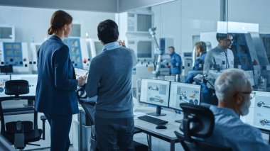 Otomotiv Tasarım Fabrikası: Proje Yöneticisi, Makine Mühendisi Konuşması, CAD Yazılım 'da 3D elektrikli araba modelini gösteren Dijital Tablet Bilgisayarı kullanın. Otomatik CNC Makineli Yüksek Teknoloji Tesisi