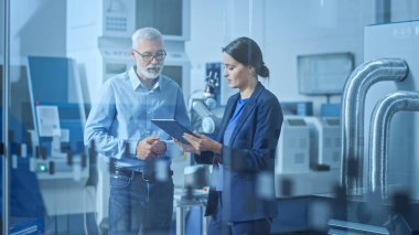 Modern Fabrika: Kadın Mühendis, Erkek Proje Yöneticisi Yüksek Teknoloji Geliştirme Tesisi, Konuşma ve Tablet Bilgisayar Kullanımı. CNC Makineli Çağdaş Tesis, Robot Arm Üretim Hattı