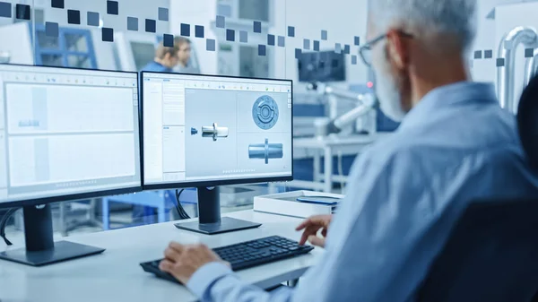 Přes rameno: Senior Heavy Industry Engineer Práce na osobním počítači, obrazovka ukazuje CAD software s 3D prototypem elektromotoru. Průmyslová továrna s high-tech CNC strojem — Stock fotografie