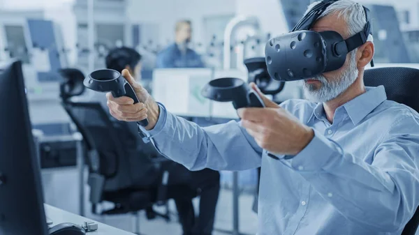 Ingeniero de diseño industrial que usa auriculares de realidad virtual y controladores de sujeción, utiliza la tecnología VR para el diseño industrial, desarrollo mediante computadora. Oficina de fábrica moderna, taller con maquinaria — Foto de Stock