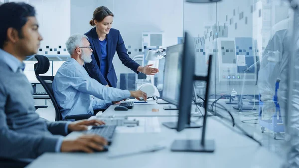 Inside Factory Office: Female Project Supervisor Talks to Male Senior Industrial Engineer who Works on Computer, Talk. In Workshop: Professional Workers Use High-Tech Industry CNC Machinery — Stock Photo, Image