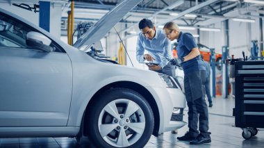 Yönetici Tablet Bilgisayardaki Tatları Kontrol Ediyor ve Kadın Tamirciye Motor Bozukluğunu Açıklıyor. Araba Servisi çalışanları LED lambayla Araç Ambarı 'nı inceliyor. Modern Temiz Atölye.