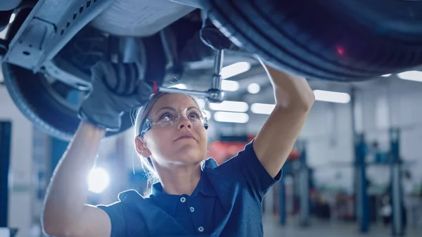 Porträtt Skott av en kvinnlig mekaniker som arbetar under fordon i en bilservice. Bemyndigande kvinna bära handskar och använda en Ratchet under bilen. Modern Clean Workshop. — Stockfoto