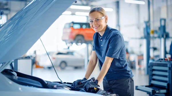 Gyönyörű empowering női autószerelő pózol a Car Service. Biztonsági szemüveget visel. Specialist Úgy néz ki, egy kamera és mosoly. — Stock Fotó