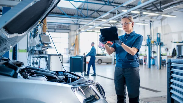 Femme mécanicien utilise un ordinateur tablette avec un logiciel de diagnostic de réalité augmentée. Spécialiste Inspection de la voiture afin de trouver des composants cassés à l'intérieur du compartiment moteur. Service de voiture moderne. — Photo