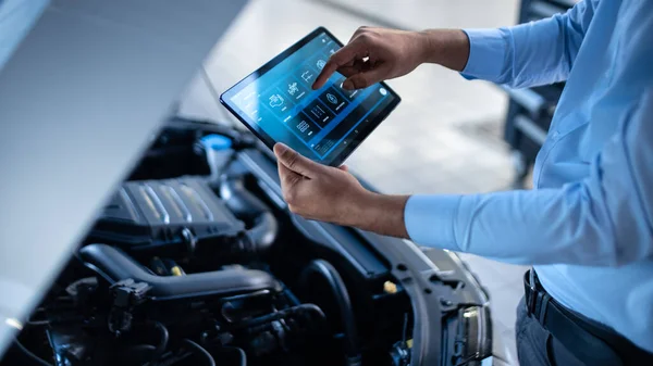 Car Service Manager or Mechanic Utiliza una Tablet Computer con un software de diagnóstico interactivo futurista. Especialista que inspecciona el vehículo para encontrar componentes rotos en la bahía del motor . — Foto de Stock