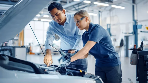 Instructor with a Tablet Computer is Giving a Task for a Future Mechanic. Female Student Inspects the Car Engine. Assistant is Checking the Cause of a Breakdown in the Vehicle in a Car Service. — Stock Photo, Image