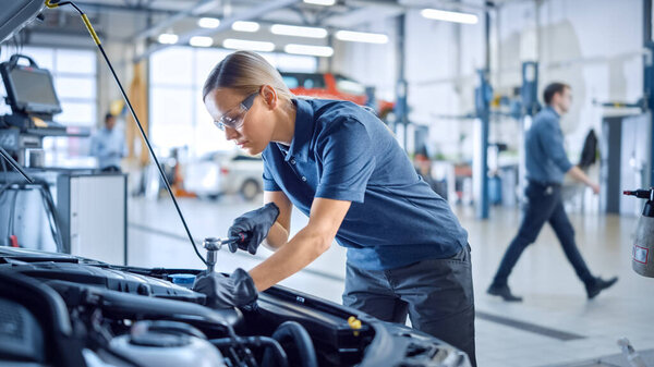 Beautiful Empowering Female Mechanic is Working on a Car in a Car Service. Woman in Safety Glasses is Working on an Usual Car Maintenance. Shes Using a Ratchet. Modern Clean Workshop with Cars.