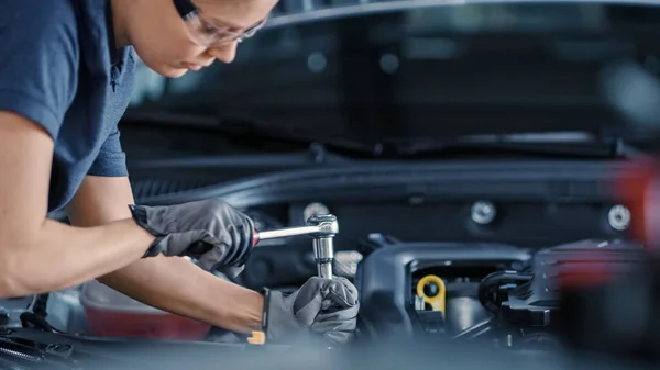 Portret kobiety mechanika pracującej nad pojazdem w serwisie samochodowym. Upoważniam kobietę do naprawy silnika. Nosi rękawiczki i używa grzechotki. Nowoczesne warsztaty Clean. — Zdjęcie stockowe