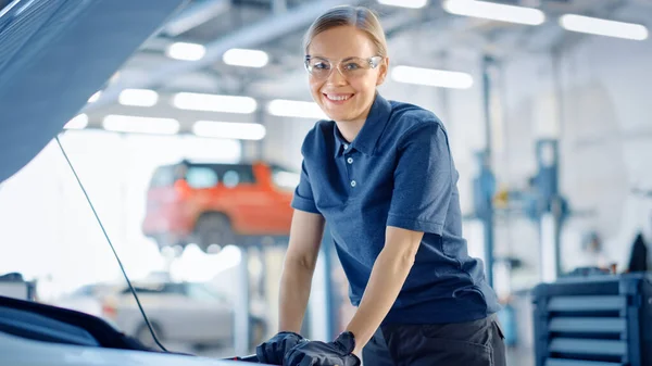 Güzel, güçlendirici kadın araba tamircisi serviste bir araç üzerinde çalışıyor. Ratchet kullanırken mutlu görünüyor. Uzman, güvenlik gözlüğü takıyor. Kameraya bakar ve gülümser.. — Stok fotoğraf