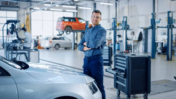 Snygg bilmekaniker är Posing in a Car Service. Han bär jeansskjorta och skyddsglasögon. Hans armar är korsade. Specialist Titta på en kamera och leenden. — Stockfoto