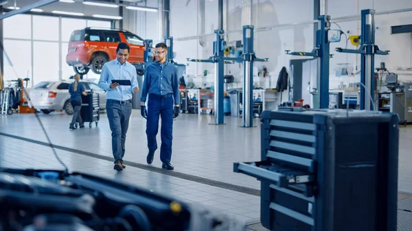 Manager Kontrollerar Diagnostik Resultat på en surfplatta Dator och förklarar ett fordon uppdelning till en snygg mekaniker. Personalen pratar medan man går i ett garage. Modern Clean Workshop. — Stockfoto