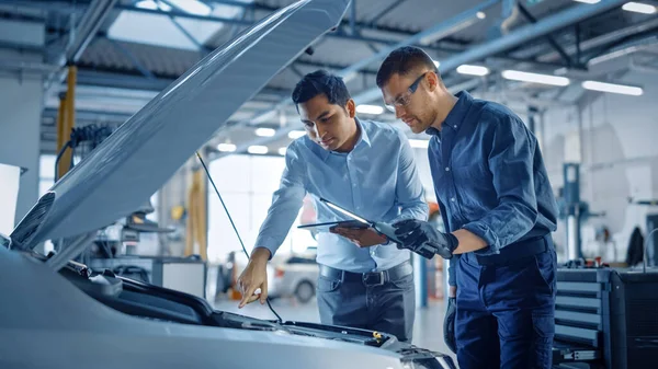 Manager Checks Diagnostics on a Tablet Computer and Explains the Engine Breakdown to a Mechanic. Car Service Employees Inspect Cars Engine Bay with a LED Lamp. Modern Clean Workshop. — Stock Photo, Image