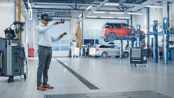 Specialist är att bära en virtuell verklighet Headset och hålla två Joysticks i en bil service. Mekaniker undersöker uppdelningen med hjälp av framtida teknik. Reparatör i modern verkstad. — Stockfoto