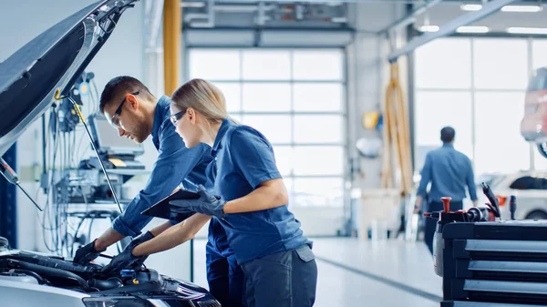 Dwóch mechaników w serwisie sprawdza samochód po otrzymaniu wyników diagnostyki. Specjalistka porównuje dane na tablecie. Naprawiający używa grzechotnika, by naprawić błędy.. — Zdjęcie stockowe