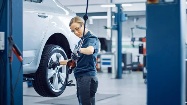 La mécanicienne blonde vérifie la pression des pneus dans une roue d'un véhicule. Autonomiser la femme travaille dans un service de voiture propre moderne. Les spécialistes gonflent la roue après avoir fixé un composant sur un véhicule. — Photo