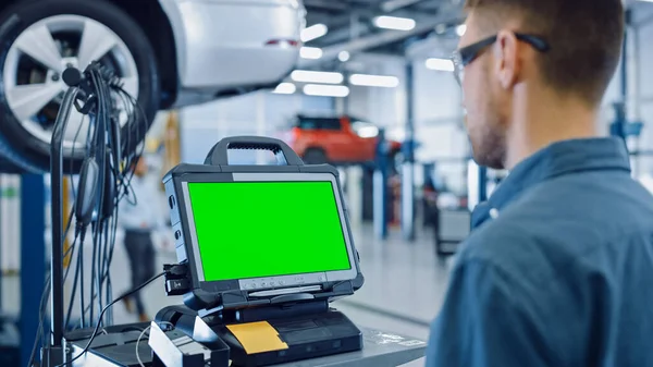 Il meccanico di servizio dell'automobile sta facendo funzionare un software di diagnostica su un calcolatore avanzato con lo schermo verde. Specialista Ispezione del veicolo al fine di trovare componenti rotti ed errori nei registri dei dati. — Foto Stock