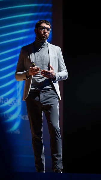 Successful Male Speaker Stands on Stage, Greets Audience and Does Presentation of the Technological Product, Shows Infographics, Statistics Animation on Screen. Start-up Conference. Vertical Photo.