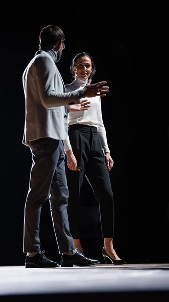 Auf der Bühne präsentieren inspirierende weibliche CEO und männliche COO-Sprecher ihr neues Produkt und sprechen über Wachstum. Live-Veranstaltung, Tech-Start-up, Business Conference. Schwarzer Hintergrund. — Stockfoto