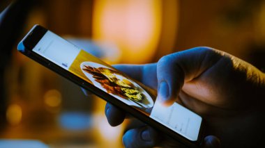 Yakın plan Macro: İnsan Tutma ve Akıllı Telefon Kullanma, Sosyal Ağ Duvarındaki Resimlere Bakma. Parmak Kaydırma Sosyal Medya Uygulaması: Seyahat, Hayvanlar, Yiyecek. Model Uygulama Tasarımı
