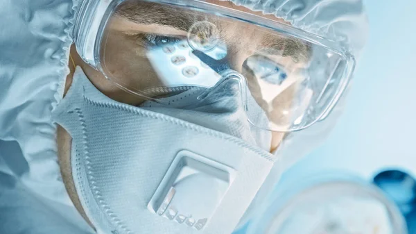Vědec nosící respirační masku, kombinézu a bezpečnostní brýle se dívá na Petriho misky s bakteriemi, tkáněmi a krevními vzorky. Laboratoř lékařského výzkumu léčí epidemické nemoci. Detailní makro — Stock fotografie