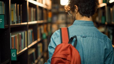 Üniversite Kütüphanesi: Sınıf Ödevi ve Sınav Hazırlıkları için Doğru Kitap Başlığı Arayan Kitap Rafları Arasında Öğrenci Yürüyüşleri. Arka Görünüm Takip Çekimi. Gençler Çalışır