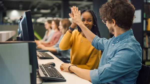 Biblioteca universitaria: Brillante ragazza nera e intelligente ragazzo ispanico insieme lavorano sui computer, dare il cinque dopo aver completato con successo il compito. Studente esame di lavoro di squadra di studio — Foto Stock