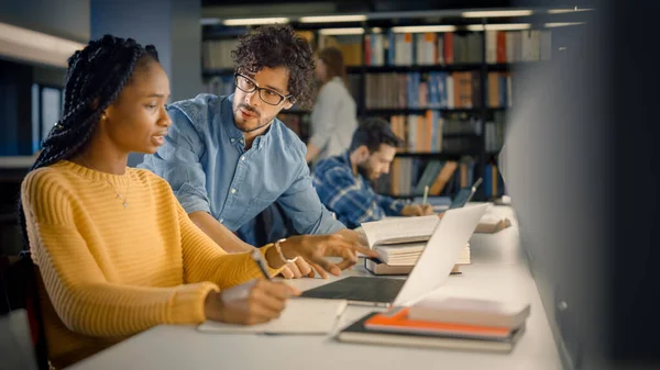 Biblioteca Universitária: Garota negra dotada usa laptop, colega de classe inteligente explica e ajuda-a com a atribuição de classe. Estudo para atribuição de papel de escrita de classe. Estudantes Diversos Aprendendo, Estudando para Exames — Fotografia de Stock