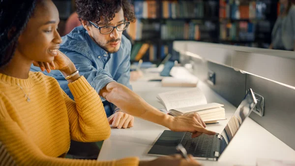 대학 도서관: 영재 흑인 소녀가 노트북을 사용하고, 똑똑 한 급우들 이 그를도와 클래스 임무를 수행 한다. 행복 한 다양 한 학생들 이 이야기하고 배우고 연구하면서 함께 연구하다 — 스톡 사진