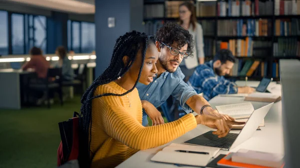 대학 도서관: 영재 흑인 소녀가 노트북을 사용하고, 똑똑 한 급우들 이 그를도와 클래스 임무를 수행 한다. 행복 한 다양 한 학생들 이 이야기하고 배우고 연구하면서 함께 연구하다 — 스톡 사진