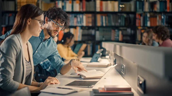 Biblioteka Uniwersytecka: utalentowana biała dziewczyna używa laptopa, inteligentny pomocny kolega wyjaśnia i doradza jej z przydziału klasy. Happy Diverse Studenci Rozmowy, Nauka, Uczenie się razem do egzaminów — Zdjęcie stockowe