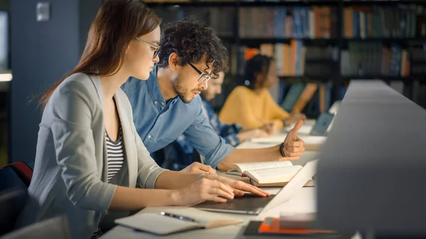 Üniversite Kütüphanesi: Yetenekli Kafkasyalı Kız Laptop, Akıllı Sınıf Arkadaşı Açıklamaları ve Sınıf Ödeviyle Ona Tavsiye Veriyor. Mutlu Çeşitli Öğrenciler Konuşuyor, Öğreniyor, Sınavlar İçin Birlikte Çalışıyor — Stok fotoğraf