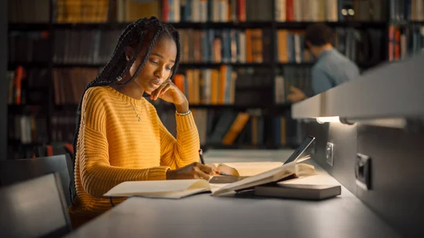 Egyetemi Könyvtár: Tehetséges Fekete Lány használja Laptop, Írja Megjegyzések a papír, Esszé, Tanulmány osztály Feladat. Diákok tanulnak, vizsgákra tanulnak. Oldalnézet Portré könyvespolcokkal — Stock Fotó