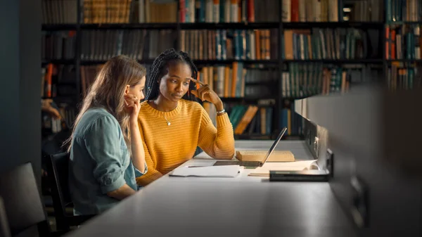 Bibliothèque de l'Université : Deux étudiantes douées étudient, utilisent un ordinateur portable, s'entraident pour obtenir des conseils, travaillent à l'affectation et se préparent aux examens. Apprentissage intelligent ciblé, Étudier pour les examens — Photo