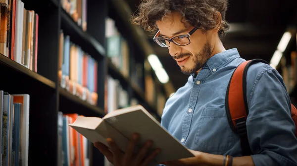 University Library: Portrait of Focused and Talented Hispanic Boy Wearing Glasses with Picked Book Title From Bookshelf for His Class Assignment and Exam Preparations. Low Angle Portrait — Stock Photo, Image