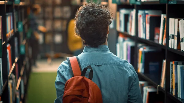 University Library: Student Walks Between Rows of Bookshelves Searching for the Right Book Title for Class Assignment and Exam Preparations. Back View Shot. Young People Study, Learn — Stock Photo, Image