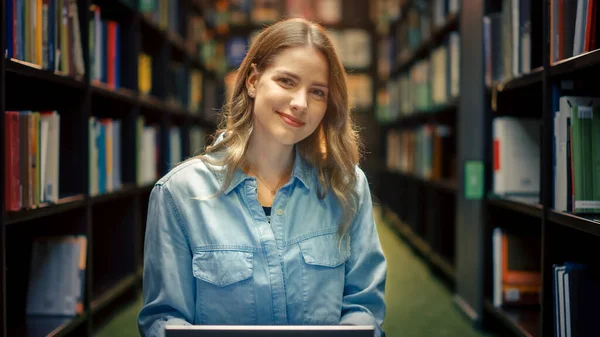 University Library Study: Portrait of Smart Beautiful Caucasian Girl Sitting Cross-Legged On Floor, Uses Laptop and Smiles Looking At Camera (en inglés). Linda chica auténtica estudios para la asignación de clase . —  Fotos de Stock