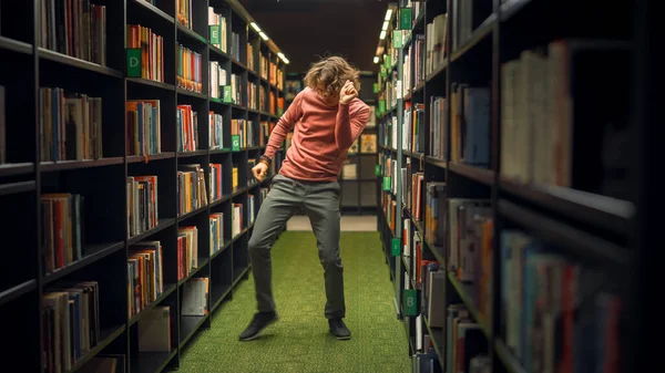 Universiteitsbibliotheek: Handsome Caucasian Student viert succesvolle Pass of Exams, Dansen tussen rijen van boekenplanken. Succes op de universiteit: Toelating, Graduations, Afwerking Master Thesis — Stockfoto