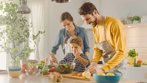 Na Cozinha: Mãe, Pai e Menino Bonito Cozinhando Juntos Jantar Saudável. Os pais ensinam o pequeno filho hábitos saudáveis e como misturar legumes na tigela de salada. bonito criança ajudando seus pais — Fotografia de Stock