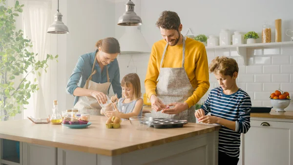 In the Kitchen: Family of Four Cooking Muffins Together. Madre e hija mezclando harina y agua para crear masa para magdalenas, padre e hijo preparando líneas de papel para sartenes. Niños ayudando a los padres —  Fotos de Stock