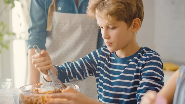 Na Cozinha: Retrato do menino inteligente bonito Misturando Farinha e Água para Criar Massa para Cupcakes. Família Cozinhar Muffins Juntos. Adoráveis crianças ajudando seus pais carinhosos — Fotografia de Stock