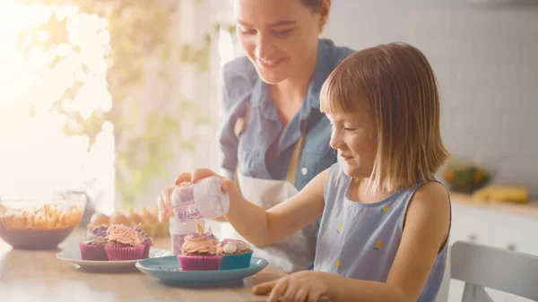 Na Cozinha: Mãe e Filha Bonita Polvilhando Funfetti em Creamy Cupcakes Frosting. Eles estão se divertindo cozinhando muffins juntos. Criança a ajudar a cuidar do pai. Tiro com filtro de luz quente . — Fotografia de Stock