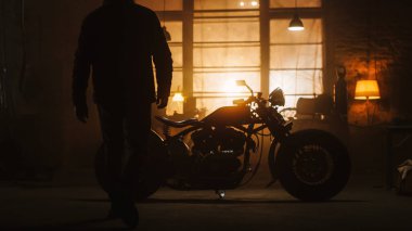 Orijinal Yaratıcı Atölye 'de duran Bobber Motosikleti. Bisiklete Gelen Bir Sürücünün Silueti. Garajda Kaliteli Motosiklet Lambası Altında.