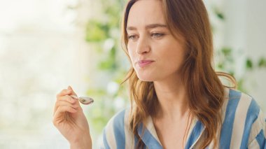 Ev Yiyen Krem Yoğurt Odasında Kaşıklı Güzel Genç Bir Kadının Otantik Portresi. Çekici Esmer Kadın Kameraya Poz Veriyor ve Nazikçe Gülümsüyor. Sağlıklı Yaşam Tarzı Olan Mutlu Kişi.