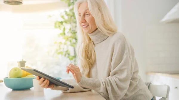 Hiteles Senior nő használja Tablet Computer Konyha szoba otthon. Gyönyörű idős nő nyugdíjas ősz hajjal szöveget ír egy Messenger egy eszközre. Idősek kéz a kézben a technológiával. — Stock Fotó