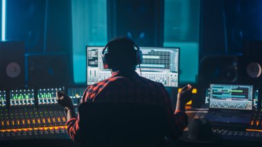 Sanatçı, Müzisyen, Ses Mühendisi, Müzik Kayıt Stüdyosunda Yapımcı, Bilgisayar Ekranı 'nda Song Playing ile Yazılım UI' sını gösteren Kontrol Masasını Kullanıyor. Yükseltilmiş Ellerle Başarı, Danslar. Arka Görünüm.