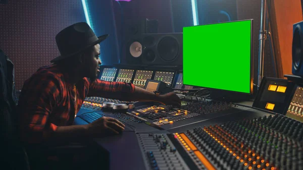 Стильный звукорежиссер, работающий в студии звукозаписи, использует клавишу Chroma с зеленым экраном, выравниватель Mixboard и пульт управления для создания нового трека и песни. Черный цвет — стоковое фото