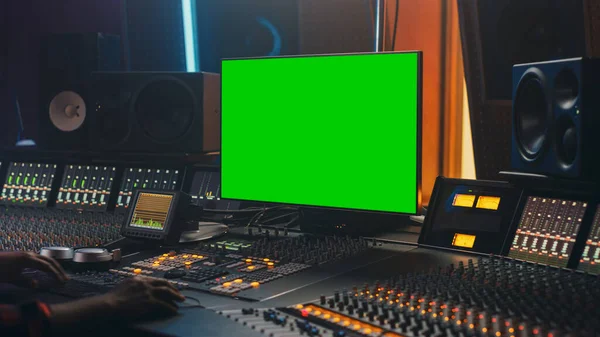 Портрет стильного звукорежиссера, работающего в студии звукозаписи, использующего зеленый экран, микро-доску, пульт управления для создания новой песни. Над плечом — стоковое фото