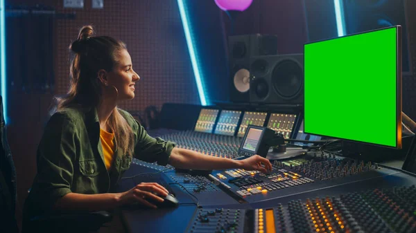 スタイリッシュな女性オーディオエンジニアプロデューサーの肖像音楽レコードスタジオで作業し、新しい曲を作成するために緑の画面コンピュータディスプレイ、ミキサーボード、コントロールデスクを使用しています。クリエイティブ・アーティスト — ストック写真